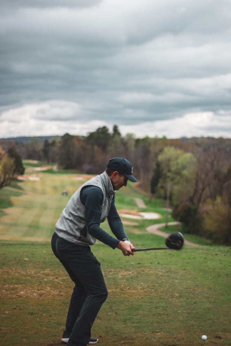 A golfer teeing off in some cold weather but supported by his nice warm clothing and winter golf pants.